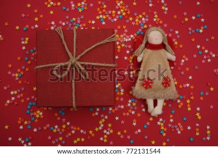 christmas holiday flying angel with wings and red paper gifts box like symbol in Christian religion or new year.picture of happy  angel toy girl with gift over red. many colorful stars