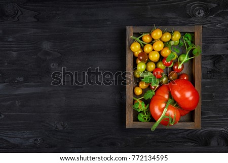Organic tomatoes of different varieties and colors in a wooden box and black texture background