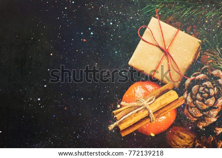Christmas Gift Box in Craft Paper Tangerine Cinnamon Sticks Fir Tree Branches Pine Cones Walnuts on Black Background Glittering Sparkling Lights Greeting Card Poster Copy Space Top View