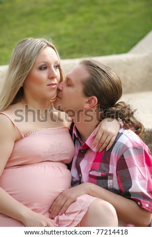 Portrait of a happy young man kisses his pregnant wife . outdoor .
