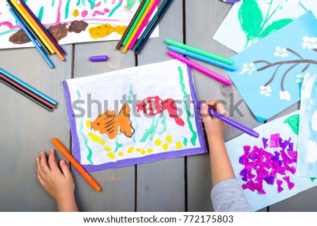 Child drawing. Top view of child hands with pencil painting picture on paper. Kid drawings