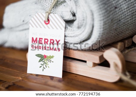 Label We wish you a Merry Christmas. Knitted white sweater on sledges. Clothes on a wooden background. Winter holidays.