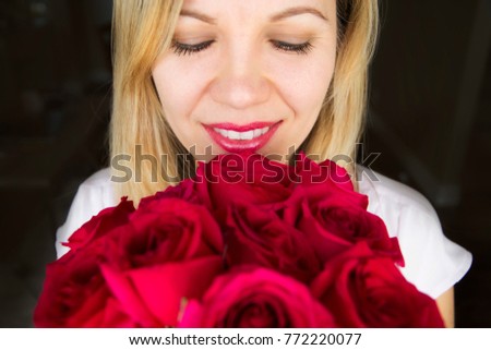 Beautiful blonde woman looking down at a bouquet of red roses, portrait