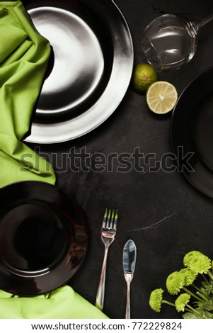Plates and cutlery on black background with contrast green color. Exquisite restaurant table setting. Art and design concept