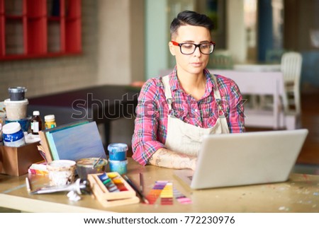 Portrait of modern tattooed woman using laptop while working in art studio, copy space