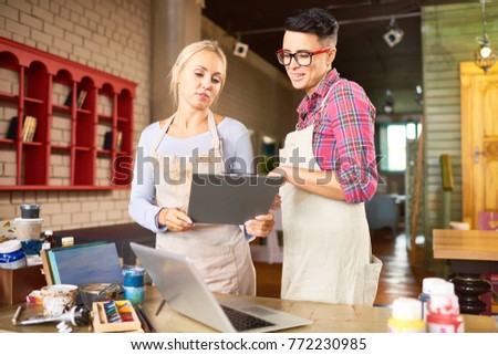 Portrait of two creative young women  working together in art studio holding clipboard and planning new  crafting project