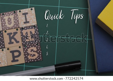 Quick Tips Concept.Book,alphabet blocks and pen with QUICK TIPS word written on a green cutting pad.