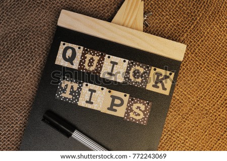 Quick Tips Concept.Book, pen and alphabet blocks with QUICK TIPS inscription on chalkboard with vintage canvas sack background.