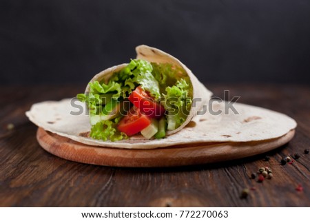  burrito with greens, cucumbers, tomatoes and sausages, on a round wooden board on a wooden background