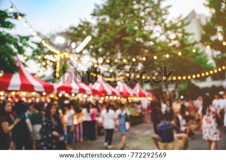 Blurred picture of Christmas festival in the park fullfill with crowd and lots of stalls for shopping with the hanging light bokeh and colorful twilight time background.