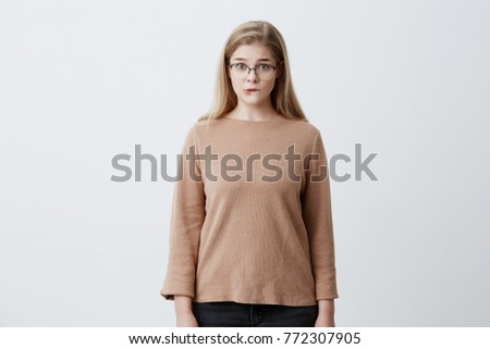 Puzzled pretty woman wearing eyeglasses with straight blonde hair biting her lower lip looking with surprise into camera. Human face expressions and emotions. European girl shocked