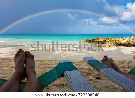 Man and woman's feet on lounge chairs at beach with ocean and rainbow