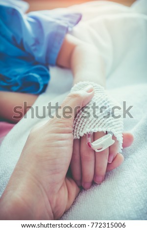 Parent holding child's patient hand for encouragement and empathy. Girl sleeping while saline intravenous drip on hand. Relationship and trust concept. Selective focus. Vintage film filter effect.
