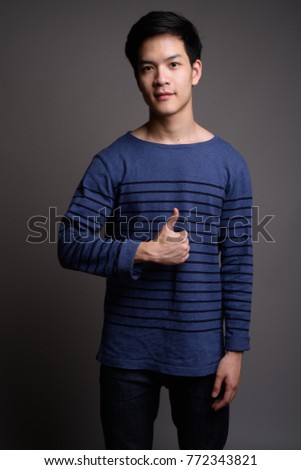 Studio shot of young handsome Asian man against gray background