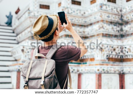 Young Asian traveling backpacker taking photos with smartphone in Wat Arun in Bangkok, Thailand