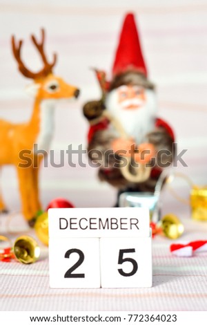 White wood block calendar on twenty fifth December with blur view background of Santa Claus,deer,gift,bell,ball for decorate Christmas party.Concept for Christmas day holiday festival.