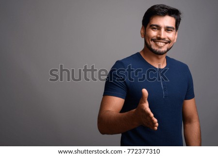 Studio shot of young handsome bearded Persian man against gray background