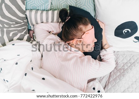 Top view of a young woman sleeping on a pillow sleeping mask on a face. Wake up for work or the day off concept. Royalty-Free Stock Photo #772422976