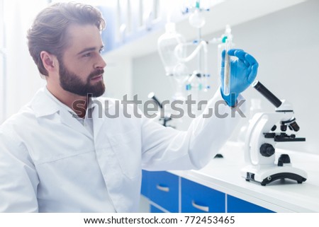 Biological research. Positive smart male biologist holding a microscope and taking a test tube while conducting a biological research