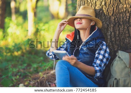 young asia woman smiling and relax listening music in headphone using a digital tablet Under the tree,Tourist traveler backpack Happy and freedom with copy space ,travel concept.