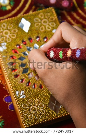 Decorated diary with pen Rajasthani handicraft Jaipur India.Child holding pen in hand to write in book adorned with lovely mirror and beads work . handy golden diary, pretty red pen. small secret book