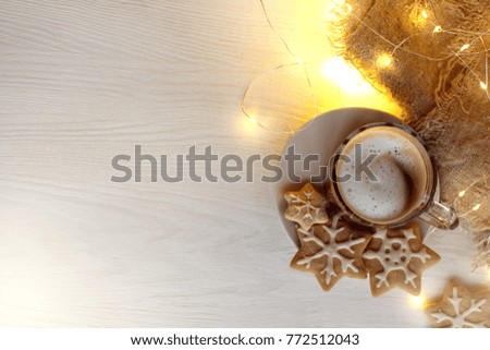 frothy cappuccino in transparent cup on a background of blurred lights garlands and figured cookies top view / festive coffee break