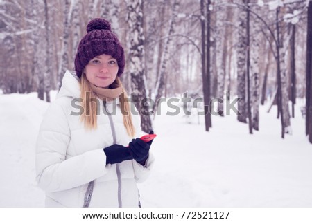 girl in a winter forest with a fashionable modern mobile phone (smartphone) in special gloves for working with a touch screen