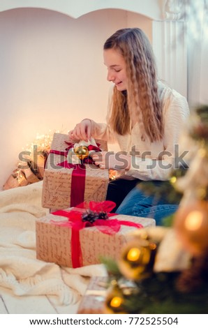 Beautiful teenage girl opening her christmas present near the christmas tree.