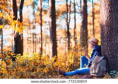 young woman relax using a digital tablet Under the tree nature park autumn sunset, Tourist traveler backpack Happy and freedom with copy space ,travel concept.