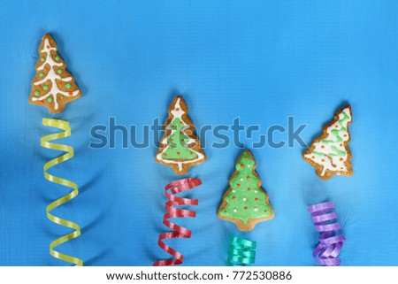 decorated ginger cookies in the form of Christmas trees fly upwards on serpentine ribbons on a blue background / abstract festive salute