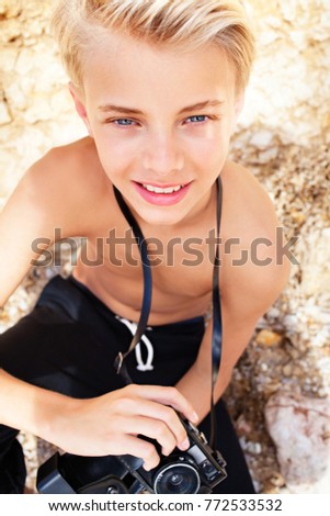 Portrait of young man on golden rock textured beach holding traditional film photo camera taking pictures on eyes looking, nature outdoors. Male teen photo hobby holiday, travel recreation lifestyle.