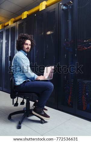 Young technician working on a laptop next to black server racks
