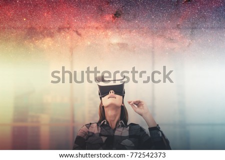 Young woman in a checkered shirt wearing VR glasses and looking upwards. A blurred office background and a sky with stars. Toned image double exposure. Elements of this image furnished by NASA