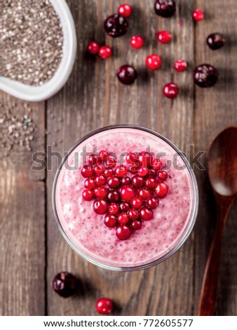 Idea for healthy breakfast on Valentine's Day: pink chia pudding with red berry puree and cranberries in shape of heart on top over wooden table background. Copy space for text Top view or flat-lay.