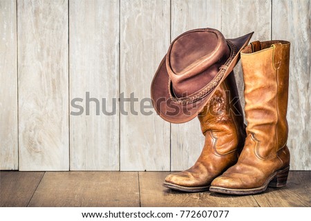 Wild West retro cowboy hat and pair of old leather boots on wooden floor. Vintage style filtered photo Royalty-Free Stock Photo #772607077