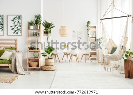 White flat interior with leaves posters and brazilian chair hanging by the window Royalty-Free Stock Photo #772619971