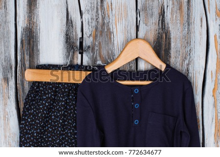 Girls garments on wooden hangers. Black floral pants and navy t-shirt with button-up neck. Rustic wooden display at the shop.