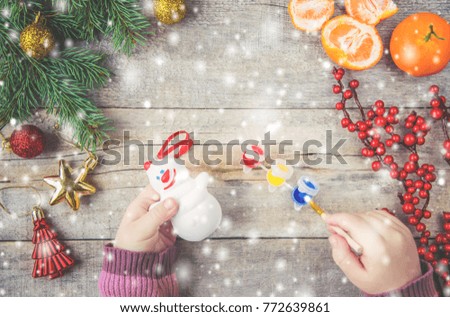 A child paints a Christmas toy, a snowman. Selective focus.