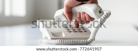 Wide panorama view of a male hand dialing a telephone number in order to make a phone call.