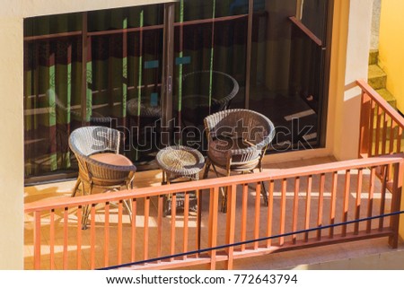 Balcony in the hotel with wicker chairs and a table. Wooden railing and large windows.
