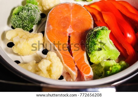 Raw salmon steak, fresh bell pepper, frozen vegetables: broccoli and cauliflower in a multi-cooker tray for steaming Royalty-Free Stock Photo #772656208