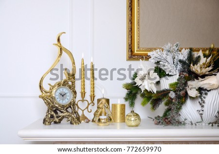 New Year and Christmas composition. Decorative golden clock, thick candles, candlestick, pot of flowers and framed canvas that hangs on the wall