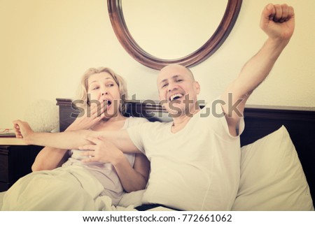 Positive mature adults lying in family bed and smiling in house