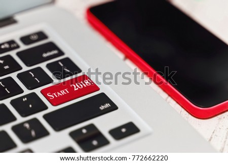 Meeting and celebrating the New Year 2018 online technologies concept. Laptop keyboard with creative tagline button instead of ENTER key and a smartphone in blur focus - close-up capture.