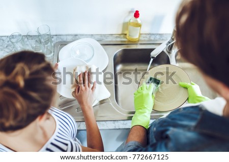 Top view of young happy couple is washing dishes while doing cleaning at home. Royalty-Free Stock Photo #772667125