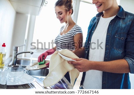 Cropped image of young happy couple is washing dishes while doing cleaning at home. Royalty-Free Stock Photo #772667146