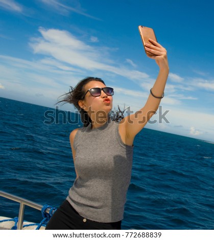 young attractive and happy Asian Chinese woman selfie portrait picture with mobile phone on boat or ferry smiling with blue sea background in holiday ship trip excursion concept
