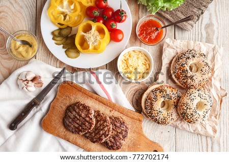 Ingredients for a delicious home burger on a wooden background. roll, bagel, with a juicy cutlet from beef, sauces cheese fresh lettuce leaves