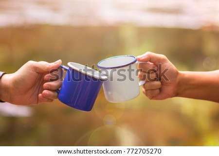 Clink glasses a cup of coffee together in the wild, blur background with sun flares