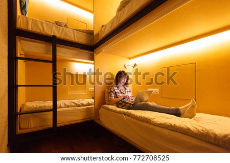Hostel for young people. Beautiful girl student working with computer lying on bed in cozy hostel Royalty-Free Stock Photo #772708525